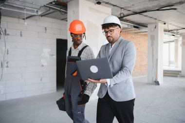 Bir inşaat sahasında proje detaylarını tartışan mimar ve inşaatçı, etkili iletişim ve planlama teknolojisinden yararlanıyor