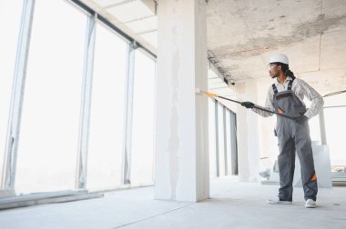 İnşaat alanında çalışan profesyonel bir ressam, uzun bir silindirle bir sütuna beyaz boya sürüyor.