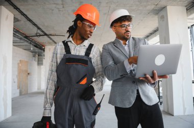 İnşaat için bina planlarını gösteren bir dizüstü bilgisayar kullanan mimar. Tulum ve inşaat halindeki bina kaskı giyiyor.