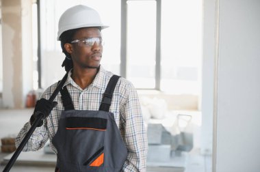 Gülümseyen Afrikalı Amerikalı inşaat işçisi inşaat halindeyken boya silindiri tutuyor..