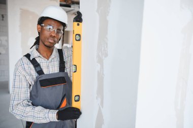 İnşaat sırasında duvarın dikey hizalanmasını sağlamak için ruh seviyesini kullanan Afrikalı Amerikalı inşaat işçisi