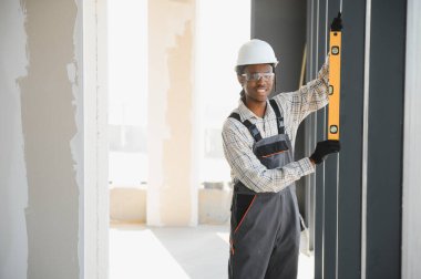 Gülümseyen Afro-Amerikan inşaat işçisi inşaat alanına pencere çerçevesi yerleştirirken ruh seviyesini kullanıyor