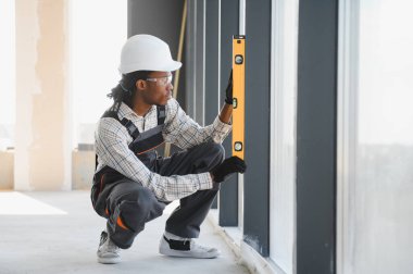 Genç Afro-Amerikan inşaat işçisi inşaat halindeki bir binanın içindeki ruh seviyesini kontrol ediyor.