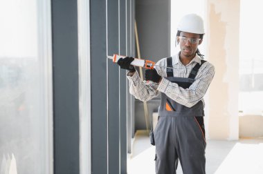 İnşaat halindeki bir binanın pencere kurulumu için silikon dolgu maddesi kullanan Afrikalı Amerikalı inşaat işçisi