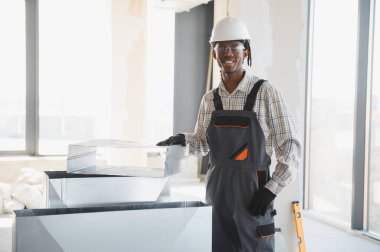 Afrikalı Amerikalı inşaat işçisi inşaat halindeki bir binaya havalandırma sistemi kuruyor.