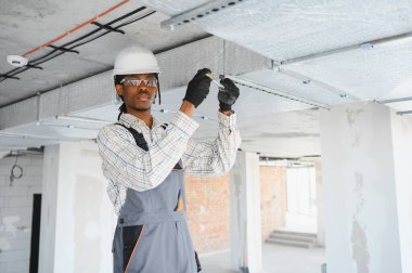 Afrika kökenli Amerikalı inşaat işçisi yoğun bir şantiyeye havalandırma sistemi kuruyor, verimli hava akışı ve konfor sağlıyor.