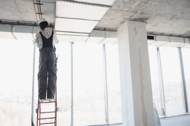 İnşaat halindeki bir binanın merdiveninde dururken havalandırma sistemi kuran Afrikalı Amerikalı inşaat işçisi.