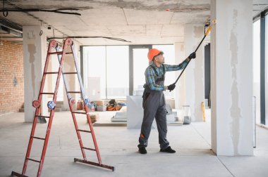 İnşaat işçisi inşaat halindeki bir binanın duvarını boyamak için uzatma çubuğu ve silindir kullanıyor.