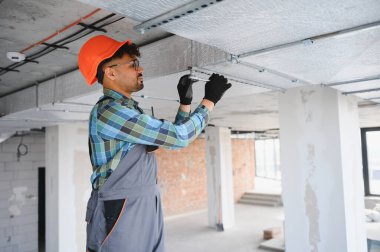 Arap mühendis, yoğun bir inşaat sahasında vidaları sıkmak için ingiliz anahtarı kullanarak özenle tavanda çalışıyor. Yetenekli işçilik sergiliyor.