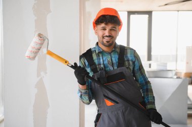 Bir inşaat sahasında çalışırken elinde boya silindiri tutan gülümseyen Arap mühendis, ev yenileme ve iyileştirme konusunda uzmanlık gösteriyor