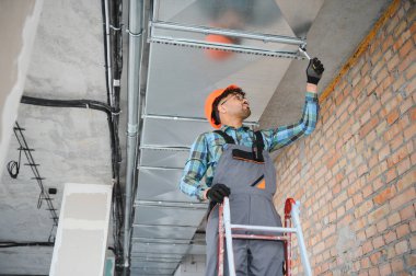 Hvac teknisyeni bir inşaat sahasında havalandırma ve havalandırma boruları üzerine çalışıyor.