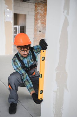 Arap inşaat işçisi bir duvarın dikey hizasını ruh seviyesini kullanarak kontrol ederek, inşaat sürecinde hassasiyet ve kesinlik sağlıyor