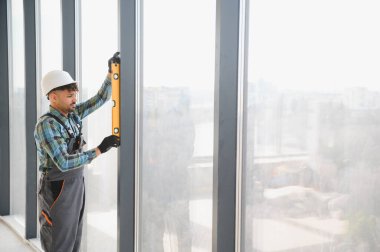 Arap inşaat işçisi, modern bir gökdelende cam kurulumunu sağlayan bir ruhsal seviye kullanıyor.