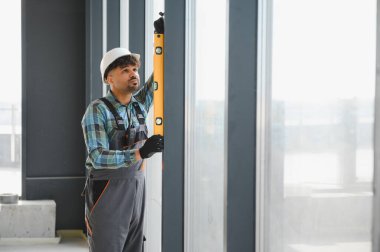 İnşaat alanındaki ruh seviyesini kullanarak pencere çerçevesinin dikey hizalanmasını kontrol eden Arap inşaatçı