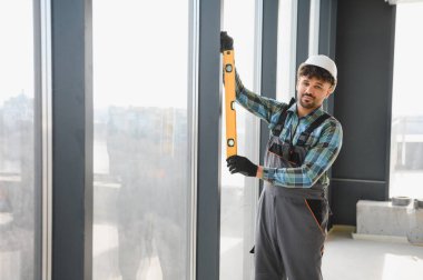 Arap inşaatçı, pencere çerçevesinin ruh seviyesini kullanarak hizalanmasını kontrol ederek, modern binada hassas kurulum sağlayarak,