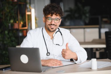 Kendine güvenen Arap doktor, modern tıp bürosunda dizüstü bilgisayarla çalışırken, başarılı bir tedavi ya da online danışma ile tatmin edici bir hareket sergiliyor