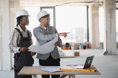 İnşaat alanında inşaatçıya bir şey gösteren mimar, ikisi de inşaat sırasında planları inceliyor.