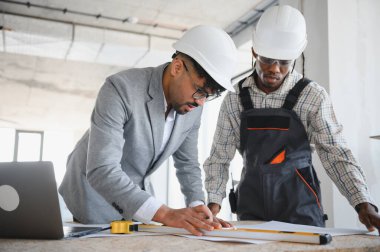 İnşaat alanında birlikte çalışan mimar ve müteahhit, planları inceliyor ve projeyi tartışıyorlar.