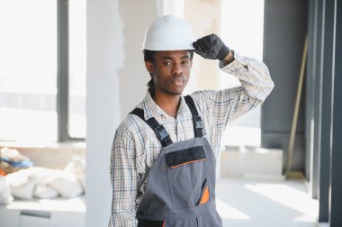 Genç Afro-Amerikan inşaat işçisi, hareketli bir inşaat sahasındaki görevlerine odaklanırken şapkasını düzelterek profesyonellik ve kararlılık gösteriyor.