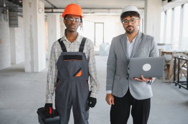 Mimar ve inşaatçı modern bir inşaat ortamında proje detaylarını tartışıyor, inşaat sektöründe takım çalışması ve çeşitliliği sergiliyor