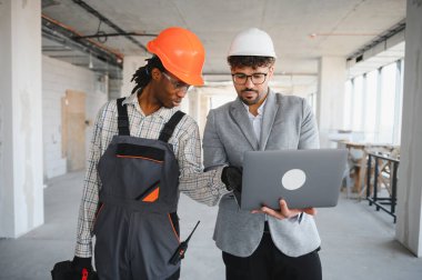 Mimar ve mimar miğfer ve koruyucu gözlük takıyor bina teftişi sırasında bir dizüstü bilgisayarda inşaat planlarını kontrol ediyorlar.