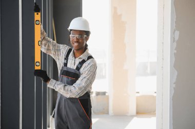 Gülümseyen Afro-Amerikan inşaat işçisi inşaat alanında çalışırken ruh seviyesini kullanıyor.