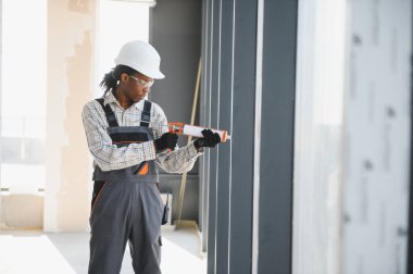 Kaliteli inşaat işçisi, pencere çerçevesine dolgu macunu sürüyor, düzgün yalıtım sağlıyor ve inşaat halindeki bir binanın inşaatını tamamlıyor.