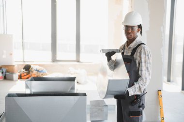 Afrikalı Amerikalı inşaat işçisi inşaat halindeki bir binaya havalandırma sistemi kuruyor.