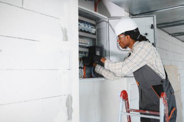 Merdivendeki elektrikçi inşaat halindeki bir binaya elektrik paneli yerleştiriyor, düzgün elektrik tesisatı ve güvenlik önlemleri sağlıyor