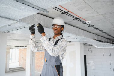 Genç Afro-Amerikan inşaat işçisi inşaat sahasına havalandırma boruları yerleştiriyor.