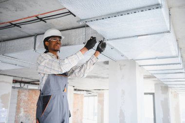 Afrika kökenli Amerikalı inşaat işçisi işlek bir şantiyeye havalandırma boruları yerleştiriyor, verimli havalandırma ve ısıtma sistemleri sağlıyor.