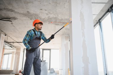 Teleskopik boya silindiri ile duvarları boyayan Arap müteahhit, güvenlik kaskı ve eldiven takarak binanın yenilenmesine odaklanıyor.