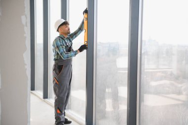 Arap inşaat işçisi inşaat halindeki bir binaya pencere çerçevesi yerleştirirken ruh seviyesini kullanıyor