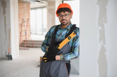 Genç Arap mühendis koruyucu iş giysisi giyiyor ve inşaat alanında dururken ruh seviyesini koruyor.