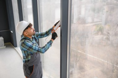 Arap inşaat işçisi, inşaat halindeki modern bir binanın geniş pencere çerçevesine silikon dolgu maddesi sürüyor