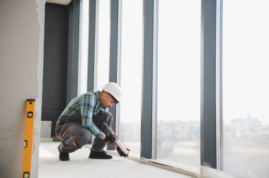 İnşaat işçisi inşaat halindeki modern bir binanın büyük bir penceresine dolgu macunu sürerek kalite ve güvenliği sağlıyor.