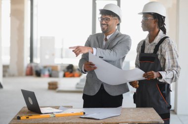 İnşaat alanının planlarını inceleyen mimar ve inşaatçı, proje detaylarını tartışıyor ve sonraki adımları planlıyor