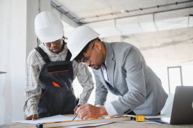 Mimar ve inşaatçı inşaat alanındaki düz bir kalem ve kalem kullanarak planlarını gözden geçiriyorlar.