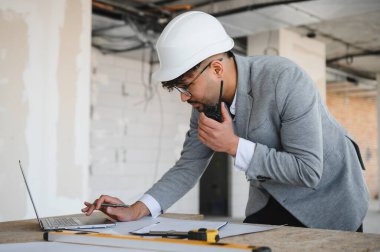 Arap mimar takım elbise giyiyor ve inşaat alanını yönetiyor, dizüstü bilgisayar ve telsiz kullanıyor.