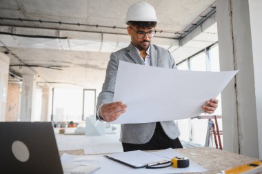 İnşaat alanının planlarını inceleyen, mimari planlar ve proje geliştirme odaklı takım elbise giyen Arap mühendis