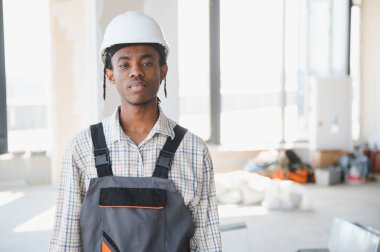 Genç Afro-Amerikan inşaat işçisi inşaat halindeki bir binada güven içinde duruyor, profesyonelliği ve beceriyi somutlaştırıyor.