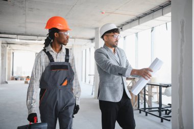 İnşaat alanında yürüyen mimar ve müteahhit, bina içinde devam eden geliştirme projesinin planlarını ve planlarını tartışıyor.