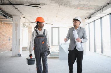 Mimarın elinde inşaat halindeki bir binanın içinde alet çantası taşıyan bir inşaatçıyla inşaat sürecini tartışan planlar var.