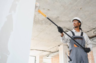 İnşaat işçisi teleskopik boya silindiri kullanıyor, duvarlara ve tavana astar takıyor, yenileme projesinde son kat için pürüzsüz yüzey sağlıyor.