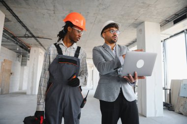 İnşaat alanında yapılan teftiş sırasında inşaatçıyla işbirliği yapan, bina planlarını dizüstü bilgisayarda gösteren, proje başarısını güvence altına alan bir mimar
