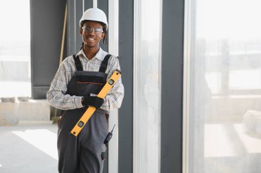 Gülümseyen Afro-Amerikan inşaat işçisi yoğun bir inşaat sahasında elinde bir aletle, uzmanlık ve profesyonellik gösterisi yapıyor.