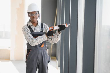 Afrikalı Amerikalı inşaat işçisi inşaat alanındaki bir pencere çerçevesine dolgu macunu sürüyor.