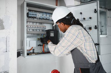 Güvenlik gözlüğü takan elektrikçi inşaat halindeki bir binanın elektrik kontrol panelini inceliyor.