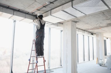 Afrikalı Amerikalı inşaat işçisi inşaat halindeki bir binanın merdiveninde dururken havalandırma sistemi kuruyor.