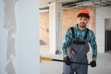 Arap inşaat işçisi turuncu bir miğfer takıyor ve inşaat alanında bir duvarı balyozla yıkıyor.